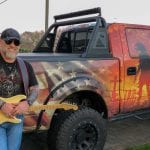 Bobby with a guitar leaning against a truck
