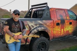 Bobby with a guitar leaning against a truck
