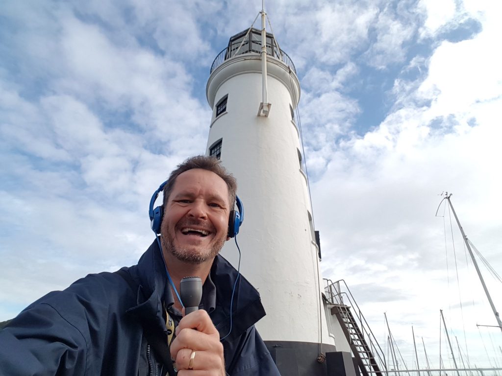 Broadcaster standing in front of a lighthouse.